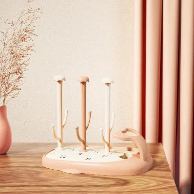 Sèche biberon CompactBébé™ en teinte pêche, avec tiges longues et design épuré, posé sur un plan de travail en bois clair dans une cuisine au décor chaleureux, idéal pour sécher les biberons et accessoires tout en optimisant l’espace.