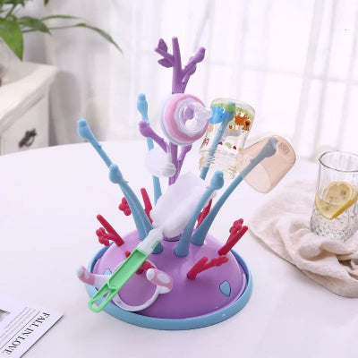 Sèche biberon à structure violette et bleue, muni d’accessoires de repas pour bébé en train de sécher dans une pièce lumineuse.

