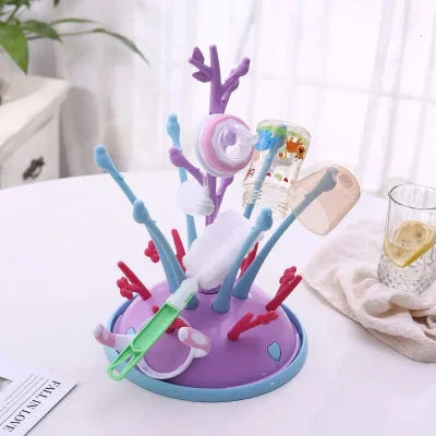 Sèche biberon à structure violette et bleue, muni d’accessoires de repas pour bébé en train de sécher dans une pièce lumineuse.


