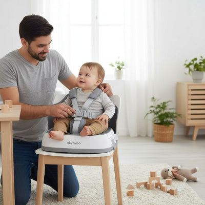 Papa attachant son bébé dans un siège repas bébé gris, réhausseur chaise enfant confortable et sûr pour repas ou jeux à la maison.