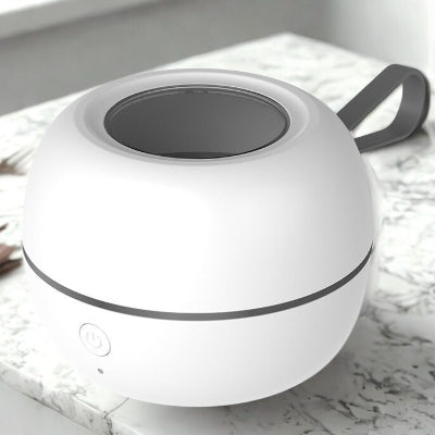Stérilisateur tétine compact blanc avec bouton d’alimentation visible et anse de transport grise, placé sur un plan de travail en marbre. Boîtier fermé au design minimaliste et moderne.