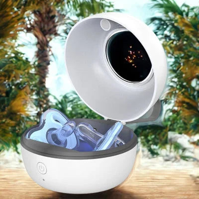 Stérilisateur tétine UV portable ouvert avec sucette à l’intérieur, posé sur une table en bois en extérieur avec palmiers en arrière-plan. Idéal pour stériliser les tétines pendant les sorties en vacances ou à la plage.