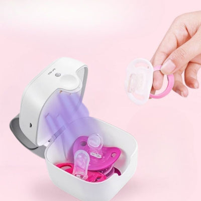 Main déposant une tétine dans le stérilisateur LumiTétine rose avec éclairage UV en action.