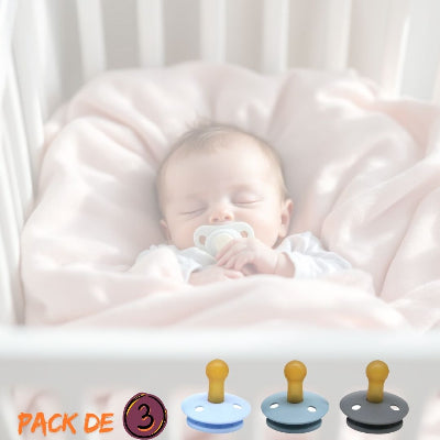 Nouveau-né endormi dans son lit avec une sucette pour nouveau-né MiniMiam™, lot de 3 tétines en caoutchouc naturel bleu, gris et anthracite, adaptées dès la naissance.