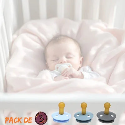 Nouveau-né endormi dans son lit avec une sucette pour nouveau-né MiniMiam™, lot de 3 tétines en caoutchouc naturel bleu, gris et anthracite, adaptées dès la naissance.